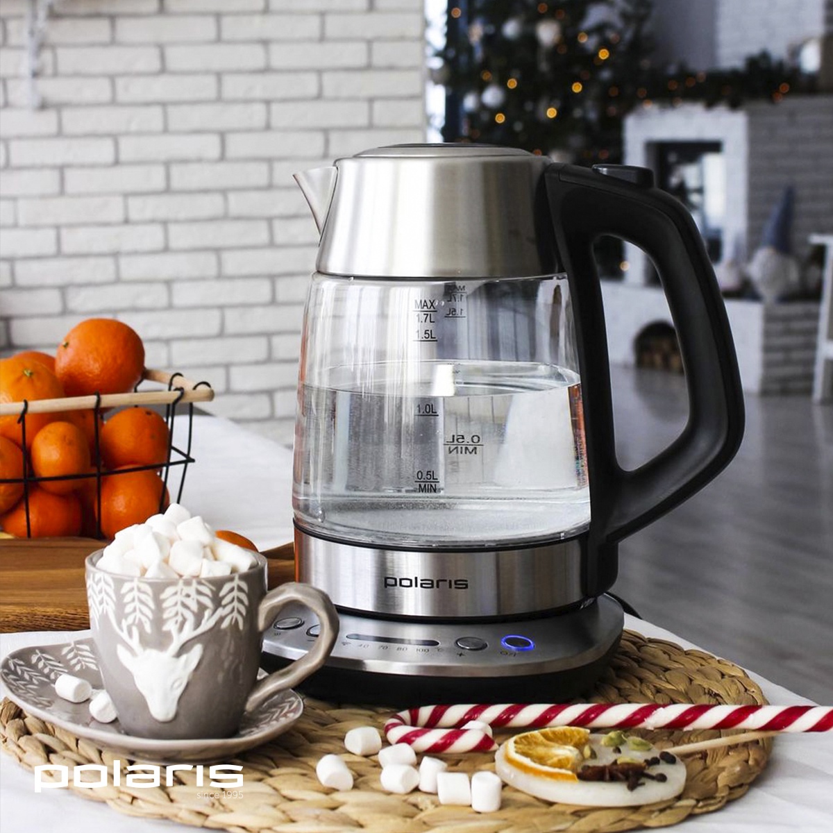 Электрический чайник Polaris стоит на столе рядом с чашкой какао и сладостями